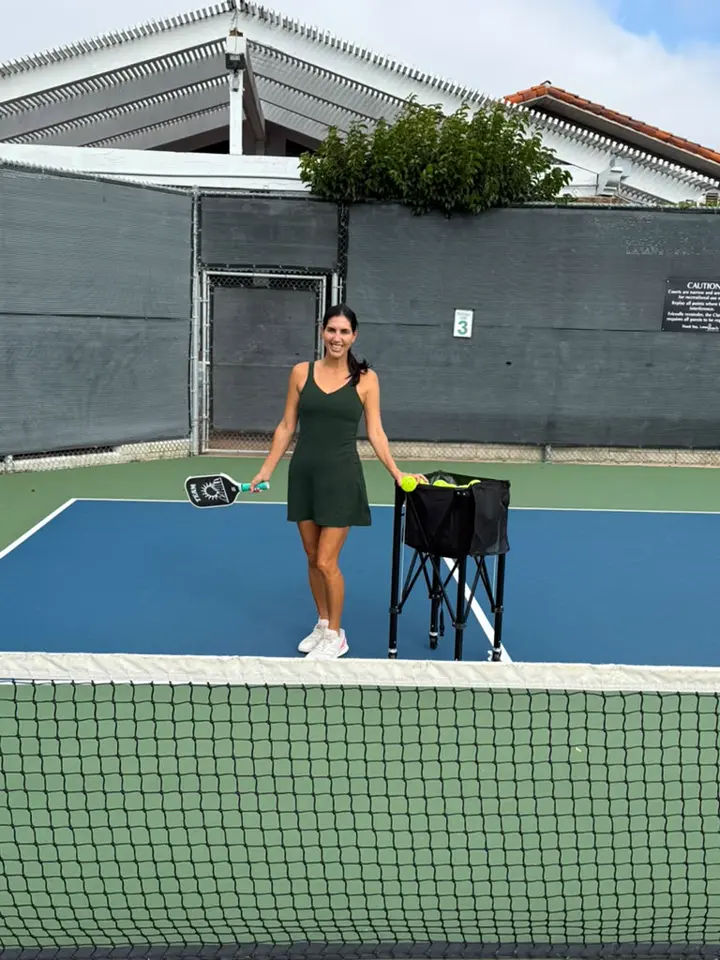 Jen on court beside a cart of practice balls