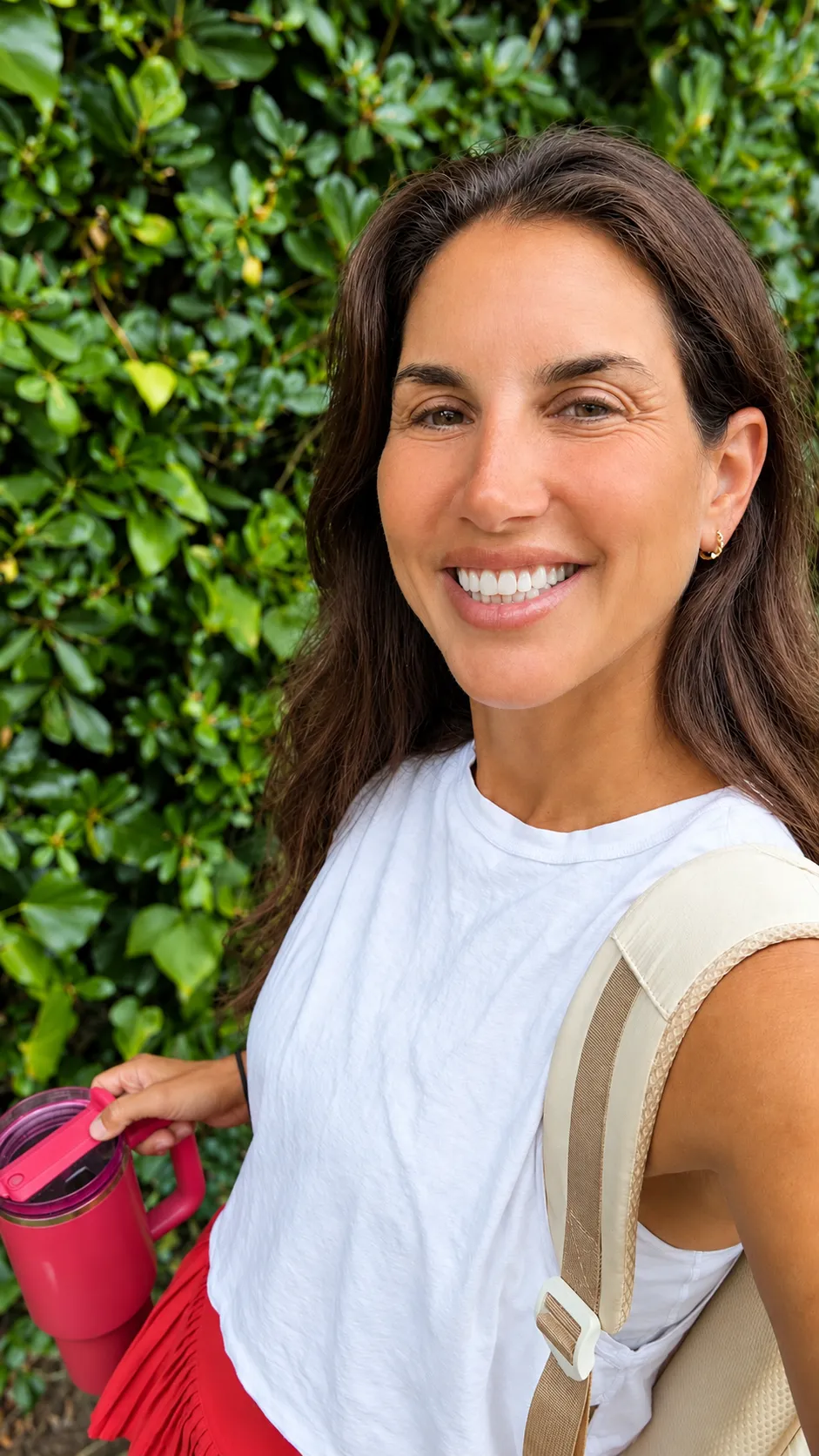 Jen smiling outdoors in front of green foliage, water tumbler in hand